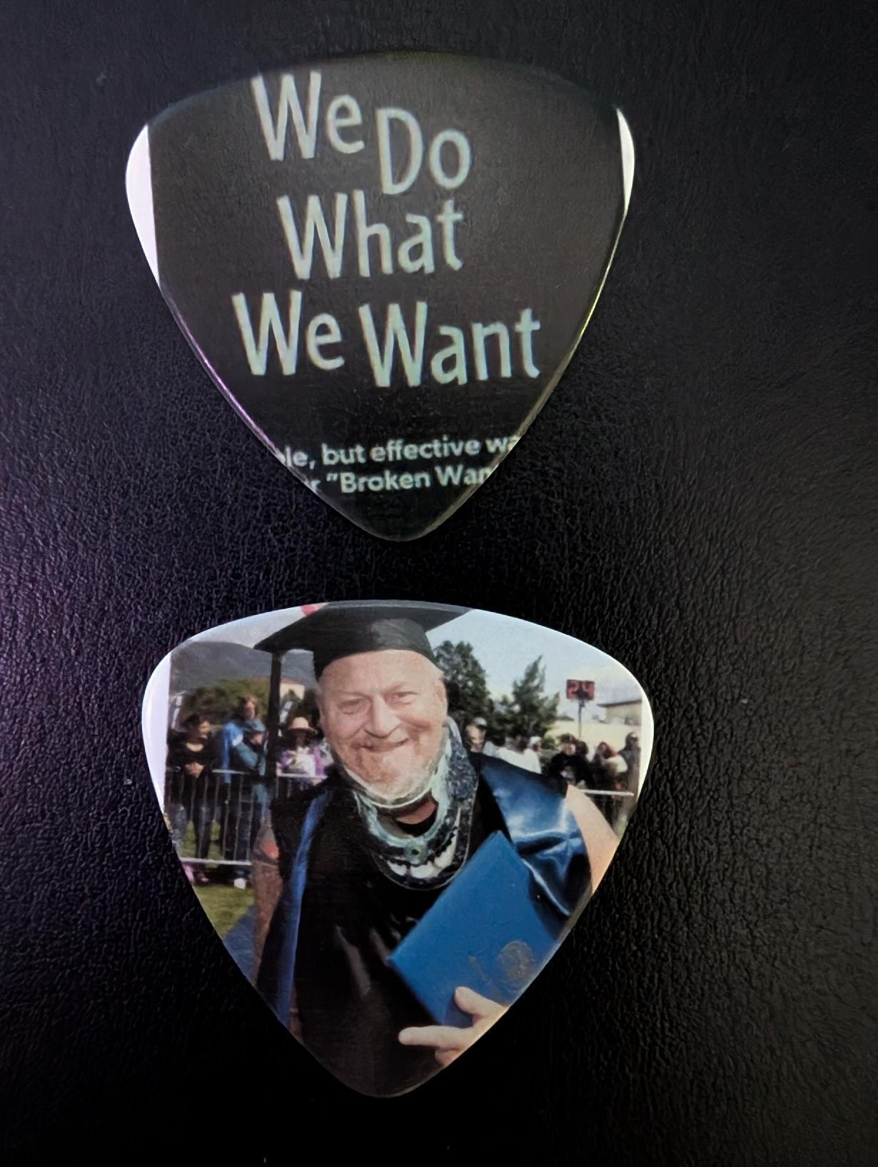 Custom Keith MF Walker guitar pick — We Do What We Want printed on one side, Keith's graduation photo on the other